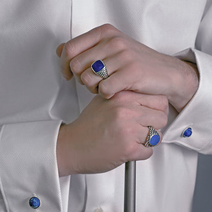 Hands wearing ALBERT M. JEWELS JEWELRY Mod. WSOX00174.TRQ rings with blue gemstones, dressed in a white shirt with matching cufflinks.