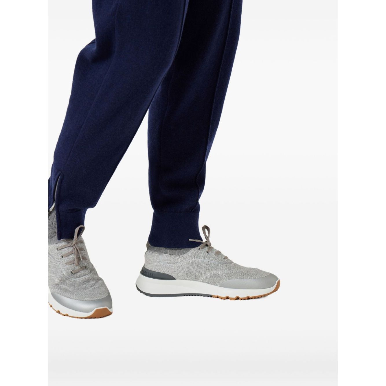 Brunello Cucinelli Techno cotton knit runners in light grey with flat sole and rubber heel, shown on a model wearing navy pants.