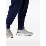 Brunello Cucinelli Techno cotton knit runners in light grey with flat sole and rubber heel, shown on a model wearing navy pants.