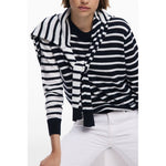 Woman wearing striped sweater with a scarf, paired with white pants.