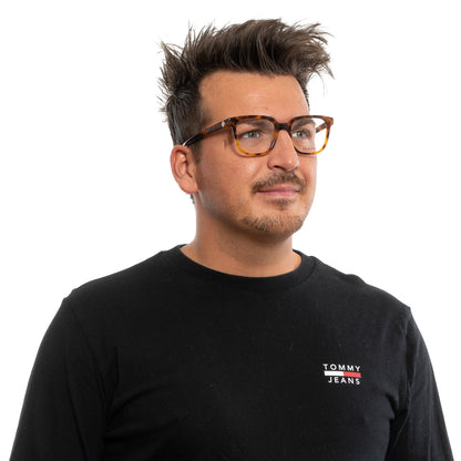 Man wearing Tommy Jeans shirt and glasses, looking thoughtful on white background.