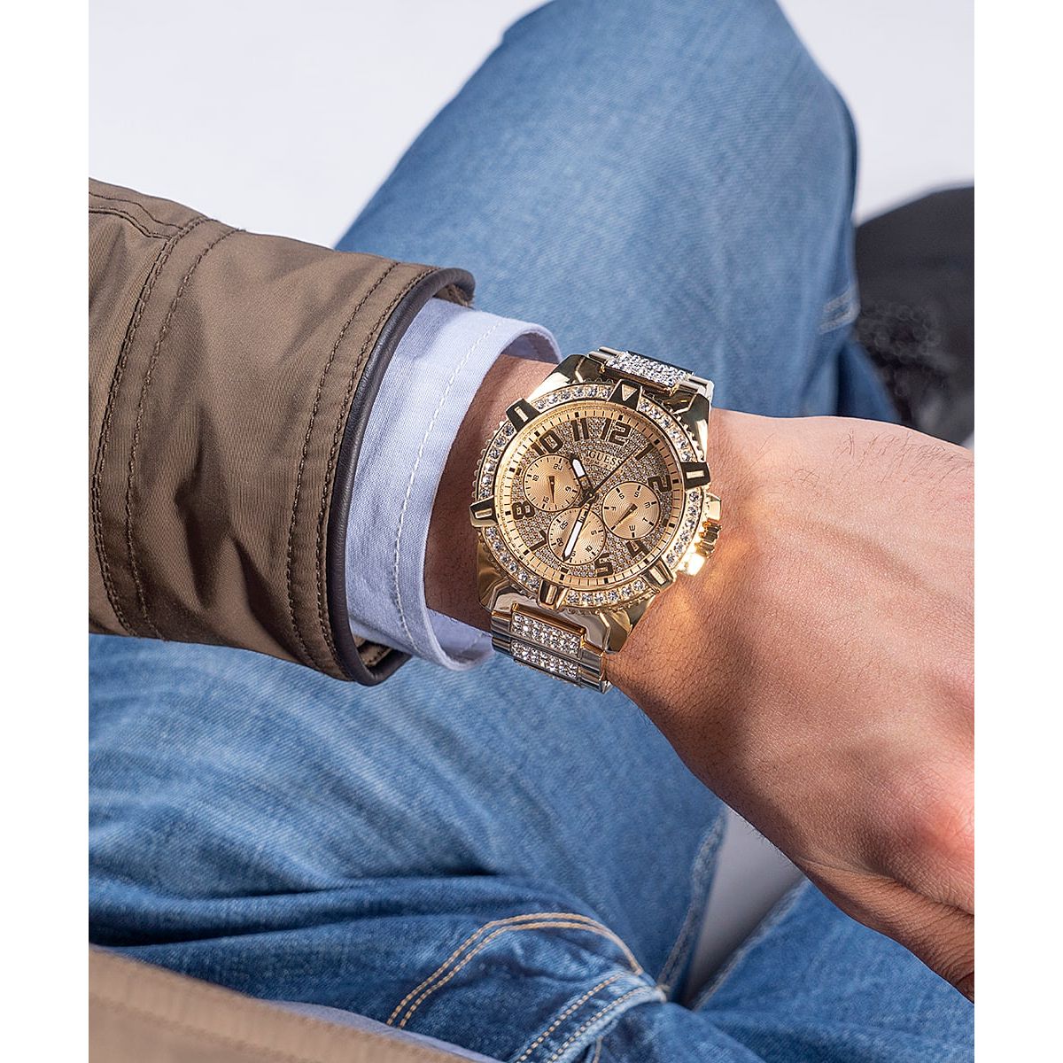 GUESS Mod. FRONTIER gold watch on wrist with brown jacket and blue jeans background