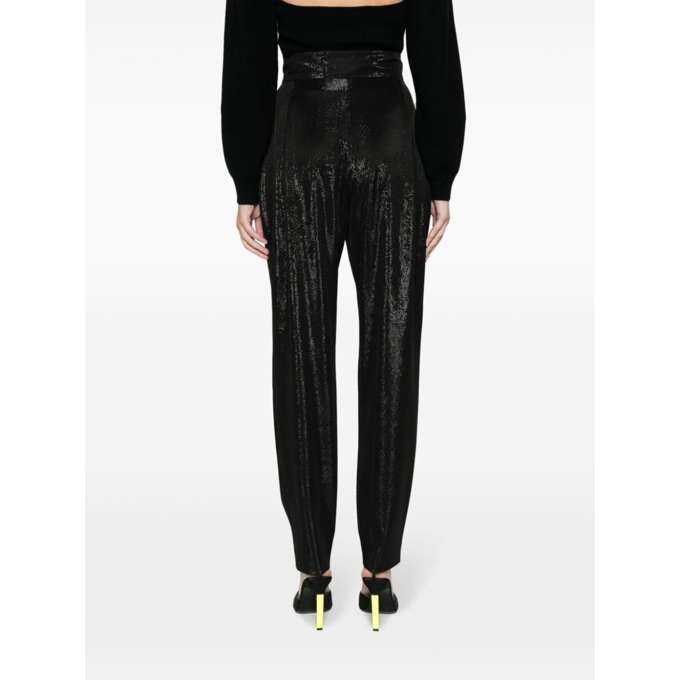 Model wearing Iro Trousers Black, high-waist straight cut with high-shine finish, two side pockets, and concealed fly in a back view.