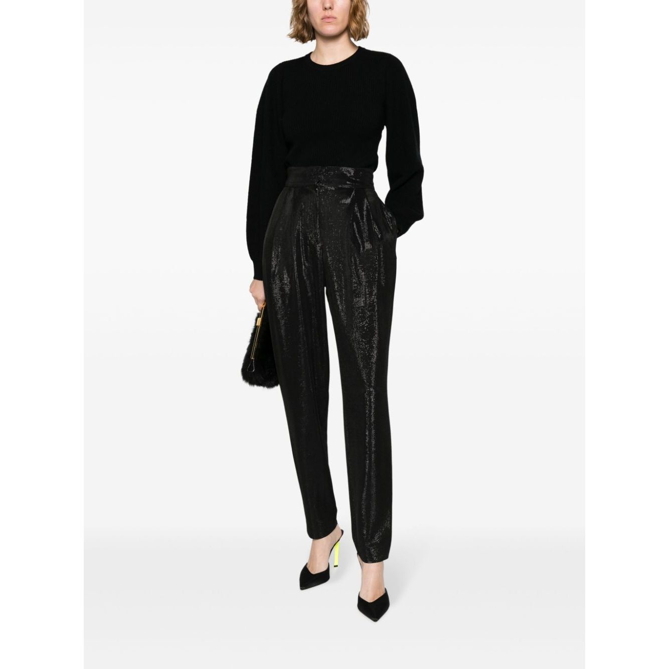 Woman wearing Iro Trousers Black, high-shine finish with high waist and side pockets, paired with black top and heels.