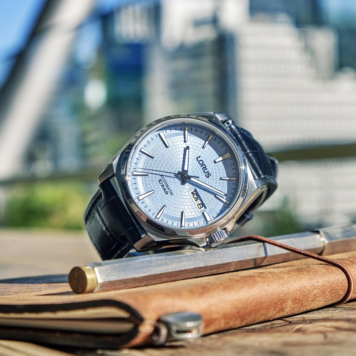 LORUS WATCHES Mod. RL417CX9 sleek silver timepiece with black leather strap displayed on a notebook outdoors