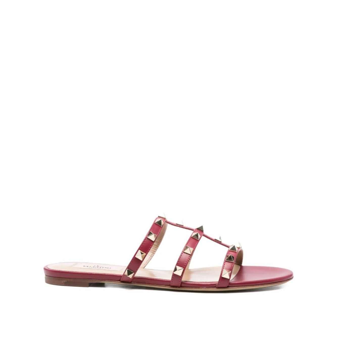 Valentino Garavani Rockstud three-strap sandals in red calf leather with Rockstud embellishments and flat sole, side view.