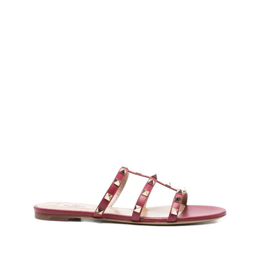 Valentino Garavani Rockstud three-strap sandals in red calf leather with Rockstud embellishments and flat sole, side view.
